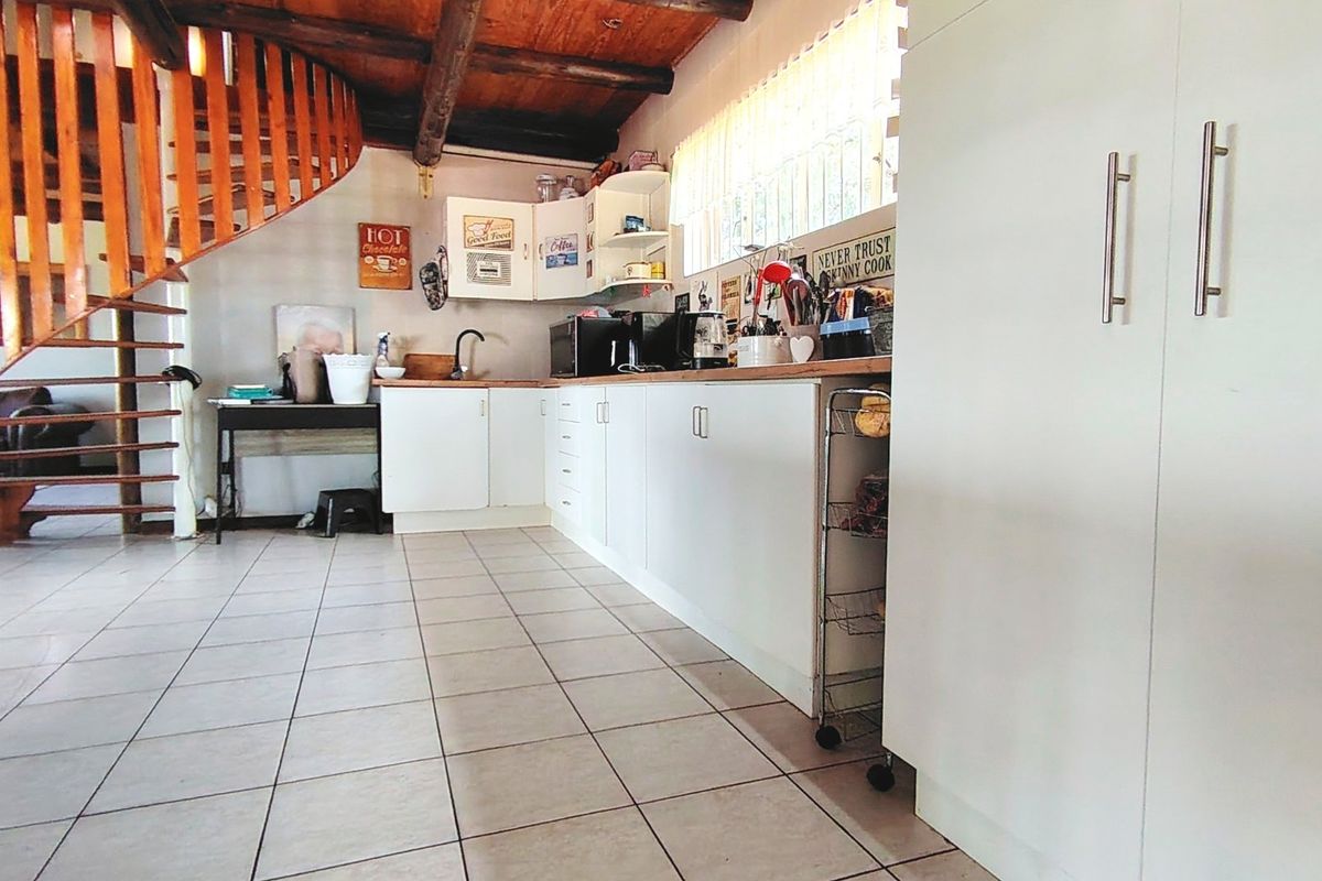 Kitchen featuring white cabinetry, tiled flooring, and exposed timber ceiling beams, with an integrated spiral staircase leading to the upper level.