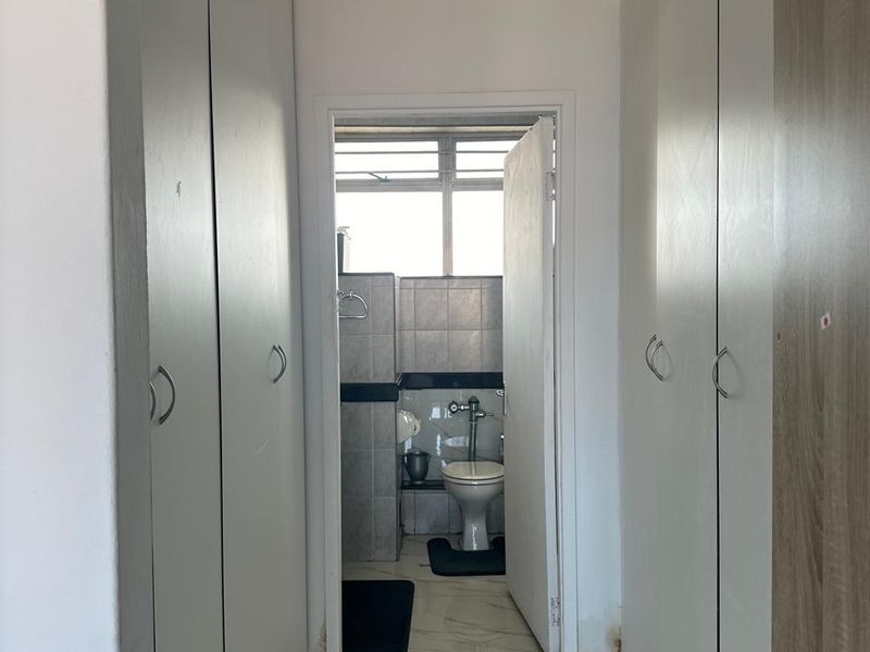 A hallway featuring extensive built-in storage cupboards with white finishes and tiled flooring, leading directly into a bathroom area.