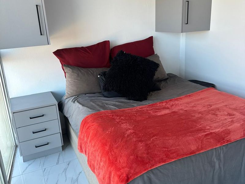 A compact bedroom featuring modern grey built-in overhead cabinetry, light-colored marble-effect floor tiles, and access to a sliding glass door.