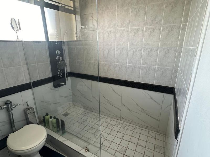 A modern bathroom featuring a walk-in shower with a glass enclosure, rainfall shower head, and contemporary wall and floor tiling.