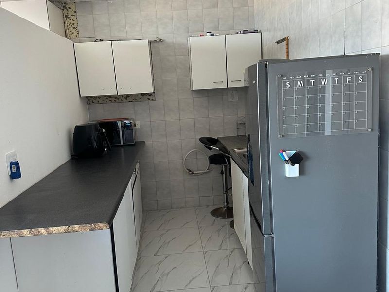 A compact kitchen featuring tiled flooring, wall-mounted cabinetry, and laminate countertops, currently showing signs of incomplete finishes and wear.
