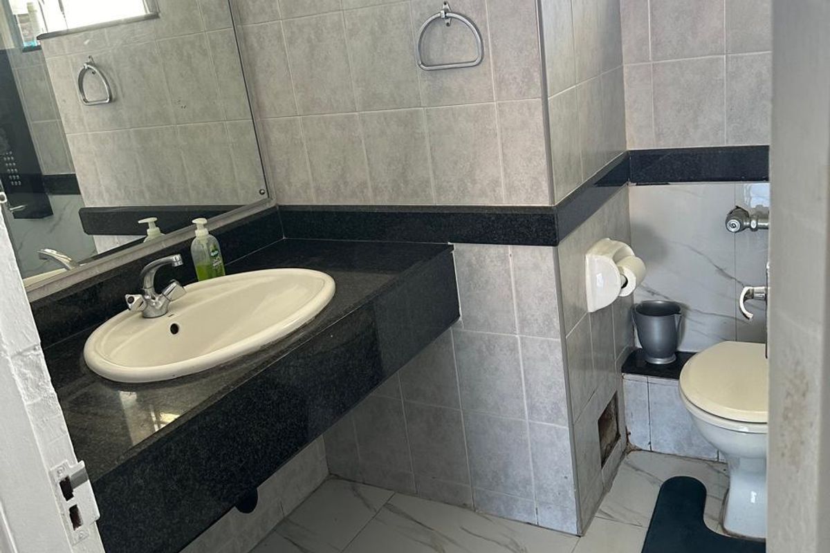 A functional bathroom featuring a granite-topped vanity, ceramic wall tiling, and a standard toilet, with a window providing natural light.