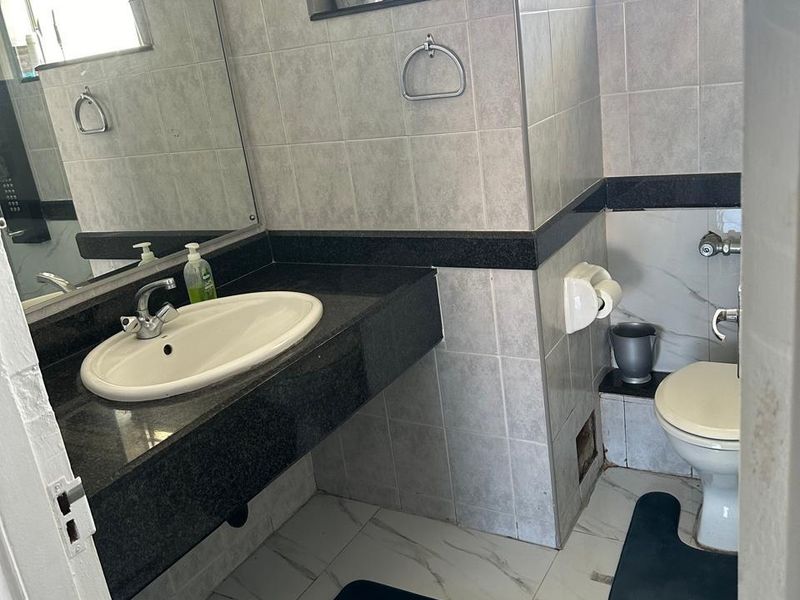 A functional bathroom featuring a granite-topped vanity, ceramic wall tiling, and a standard toilet, with a window providing natural light.