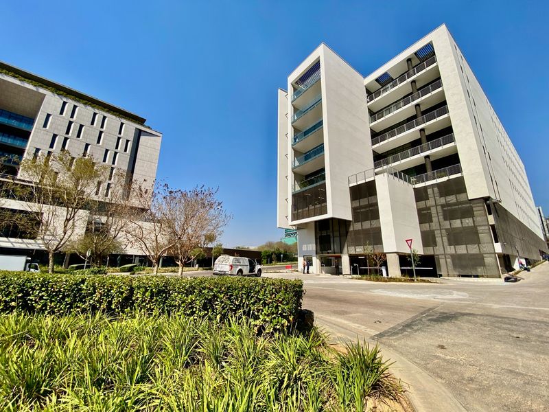 Modern multi-story commercial building featuring glass balconies and metal mesh facade elements, situated in a well-maintained business park setting.