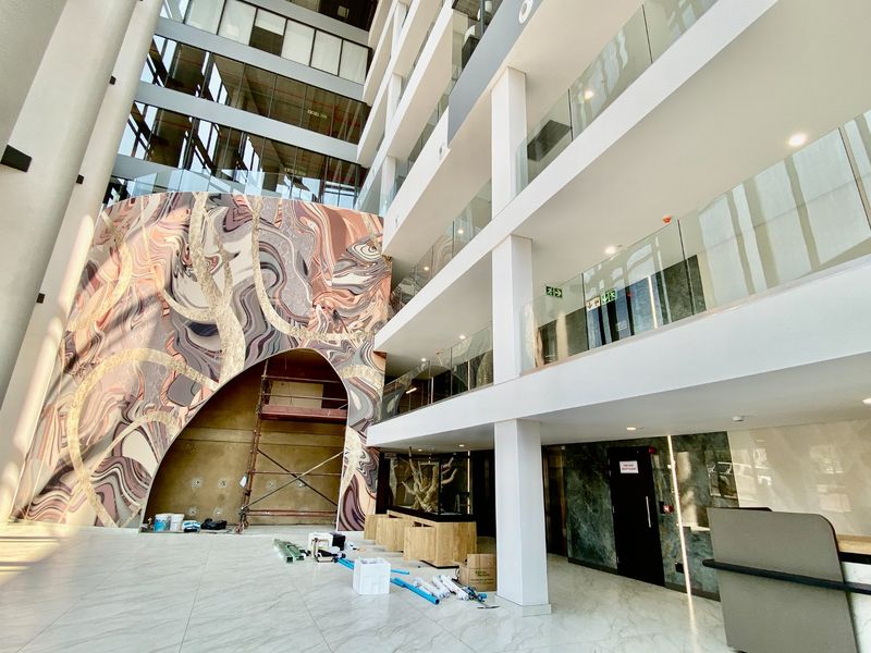 Spacious commercial atrium entrance featuring high ceilings, glass balustrades, marble-look flooring, and a striking decorative feature wall under construction.