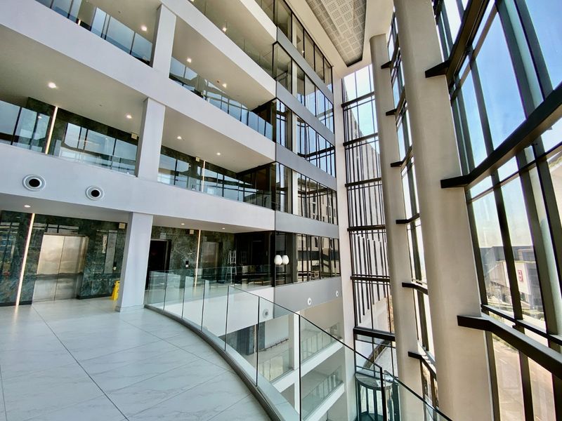 Modern multi-level commercial atrium featuring expansive floor-to-ceiling glass windows, marble-clad elevator lobby, and sleek glass balustrades in a bright, open-plan architectural design.