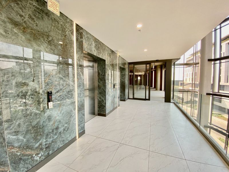 Modern commercial elevator lobby featuring premium marble wall cladding, large format floor tiles, and expansive floor-to-ceiling glass windows providing natural light.