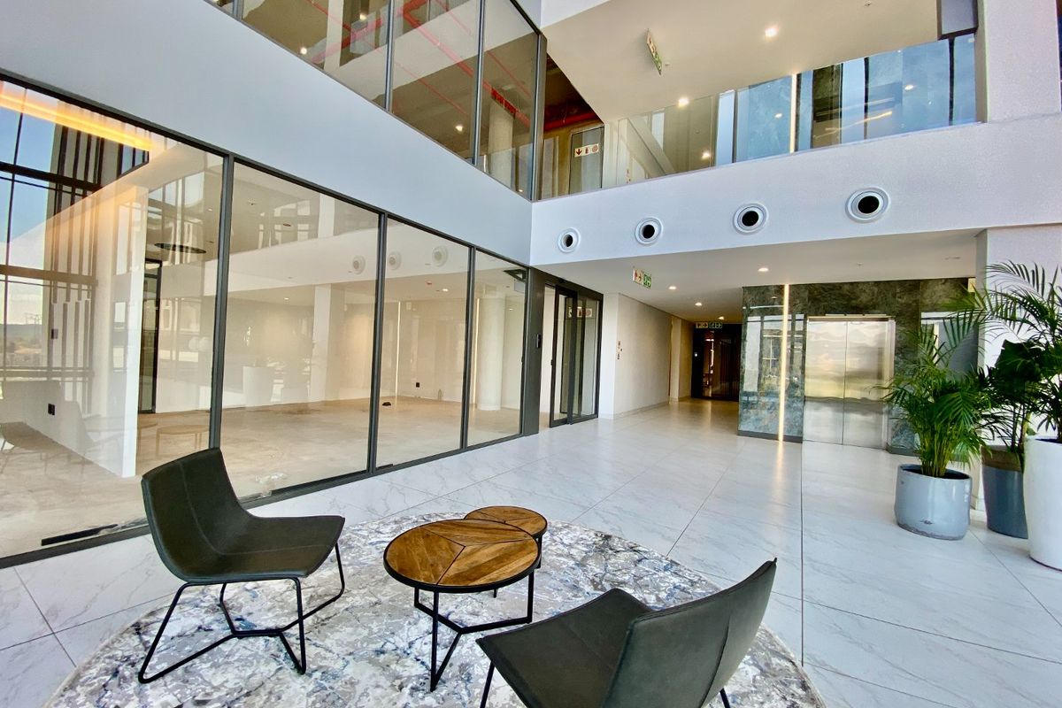 Modern commercial building entrance lobby featuring high ceilings, glass-partitioned office spaces, polished tile flooring, and a built-in elevator.