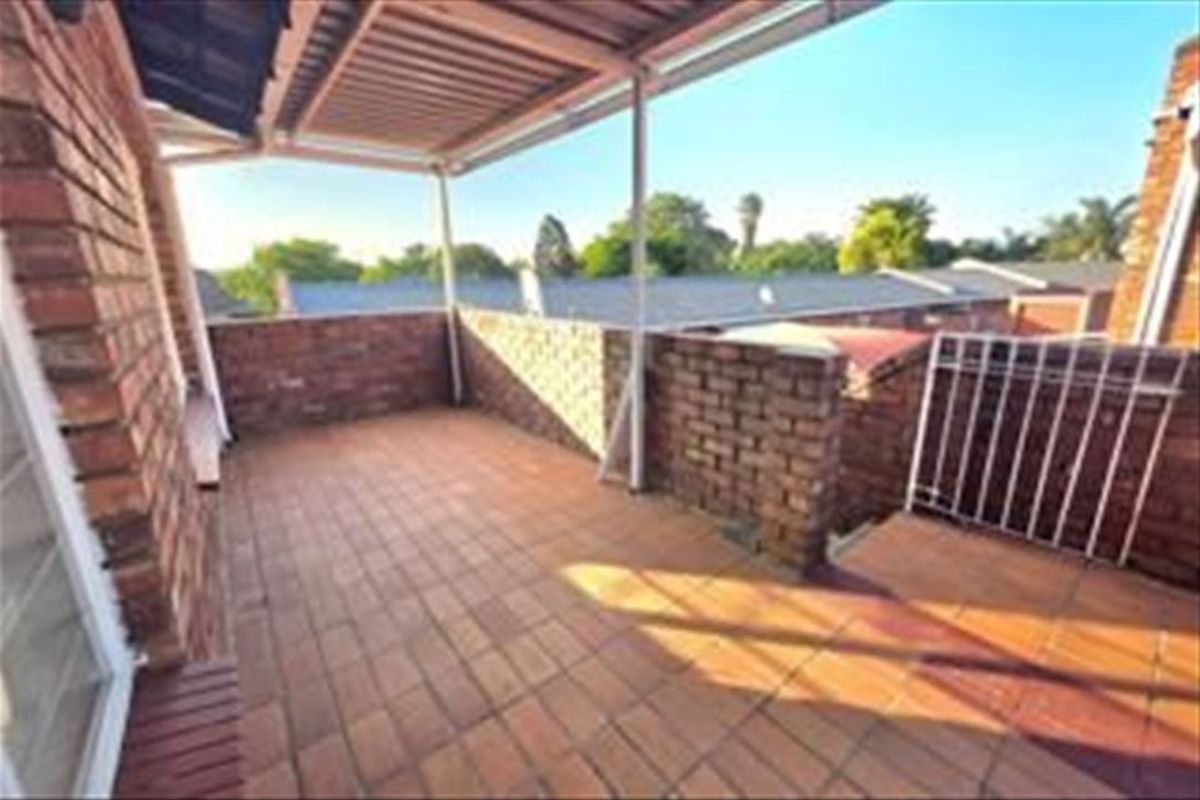 A covered outdoor balcony featuring brick walls, tiled flooring, and a metal roof structure, offering an open-air space for relaxation.