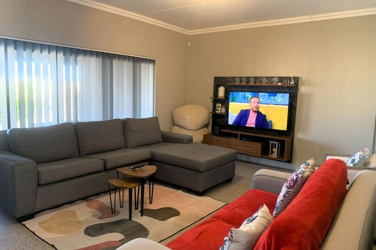 A comfortable living room featuring a built-in media unit, crown molding, and large windows with vertical blinds.