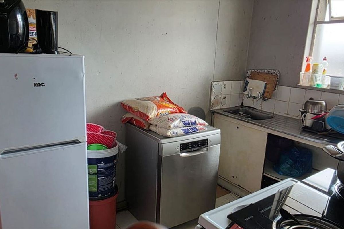 A compact kitchen area featuring a stainless steel sink, tiled splashback, and built-in cabinetry, currently showing signs of wear and requiring maintenance.