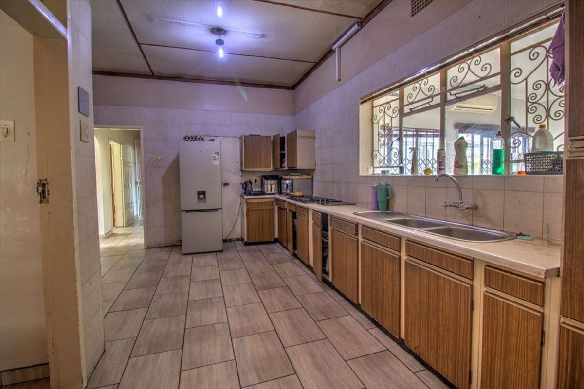 A dated kitchen featuring wood-finish cabinetry, tiled countertops, a double sink, and a built-in hob, with tiled flooring throughout.