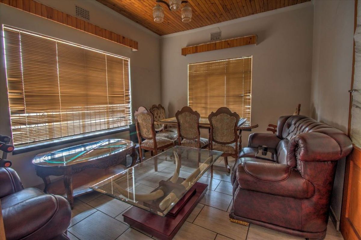 A living and dining area featuring tiled flooring, timber ceiling paneling, and large windows with fitted blinds.