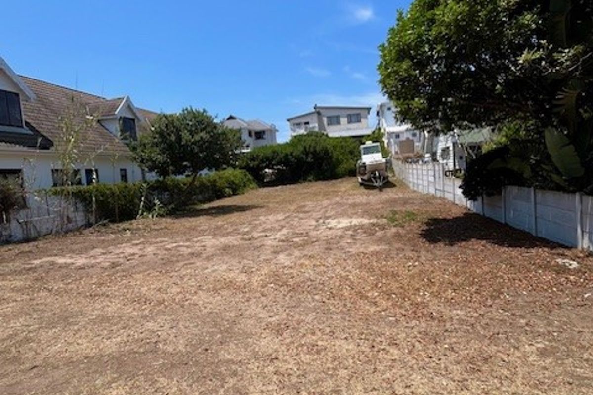 A vacant residential plot of land featuring boundary fencing and mature trees, offering a clear space ready for development.