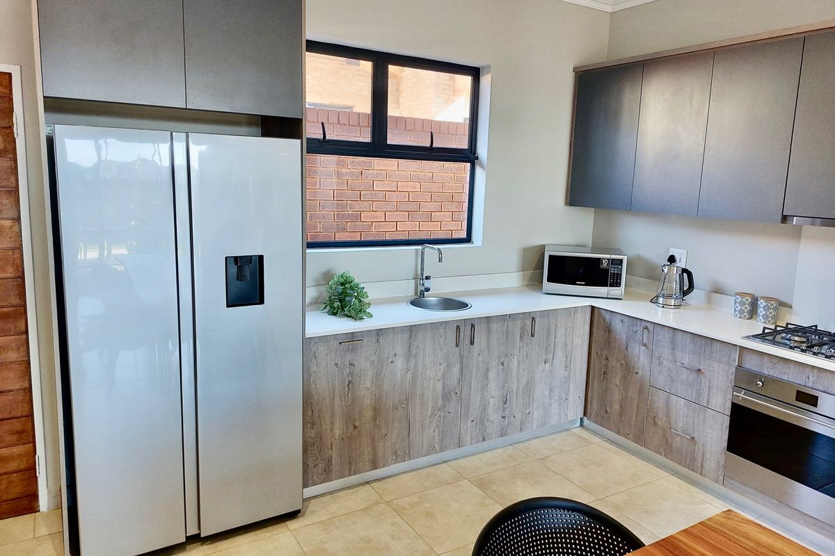 Modern kitchen featuring wood-grain cabinetry, stone countertops, integrated oven, gas hob, and a sleek undermount sink with a contemporary mixer tap.