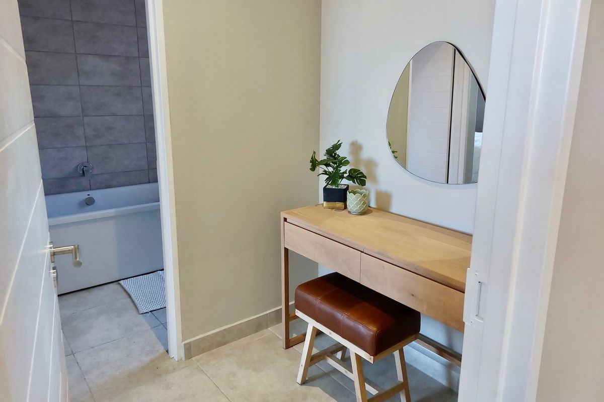A modern bathroom featuring a built-in bathtub with grey tiled wall accents and neutral floor tiles, adjacent to a dressing area.