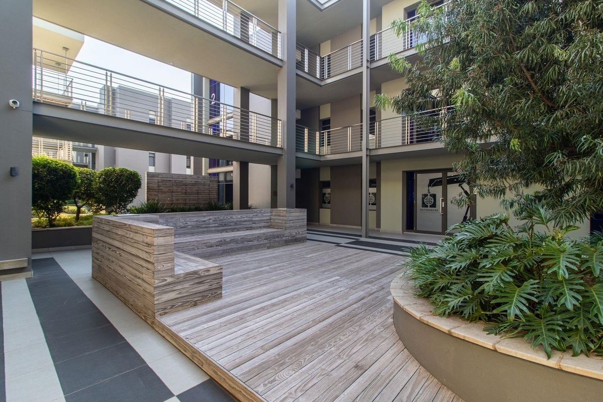 A modern commercial courtyard featuring timber decking, built-in seating, and multi-level walkways with metal balustrades, providing an open-air communal space.