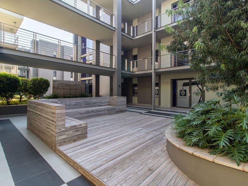 A modern commercial courtyard featuring timber decking, built-in seating, and multi-level walkways with metal balustrades, providing an open-air communal space.