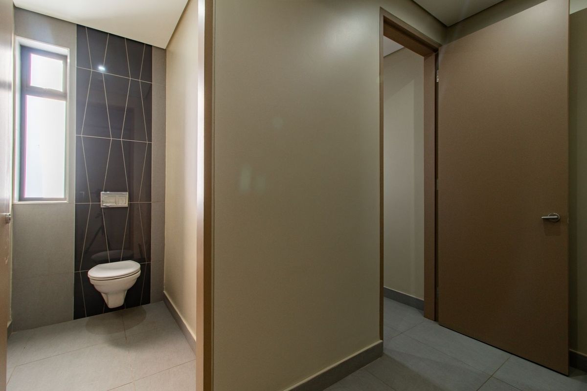 A modern, minimalist bathroom featuring a wall-mounted toilet with a concealed cistern, accented by a dark tiled feature wall and neutral floor tiles.