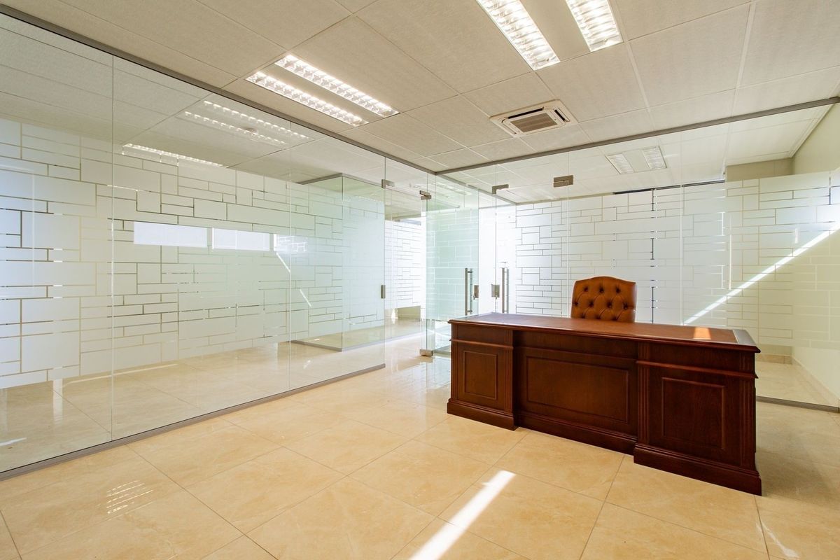 Modern commercial office space featuring glass partition walls with frosted detailing, ceramic tiled flooring, and integrated ceiling lighting.