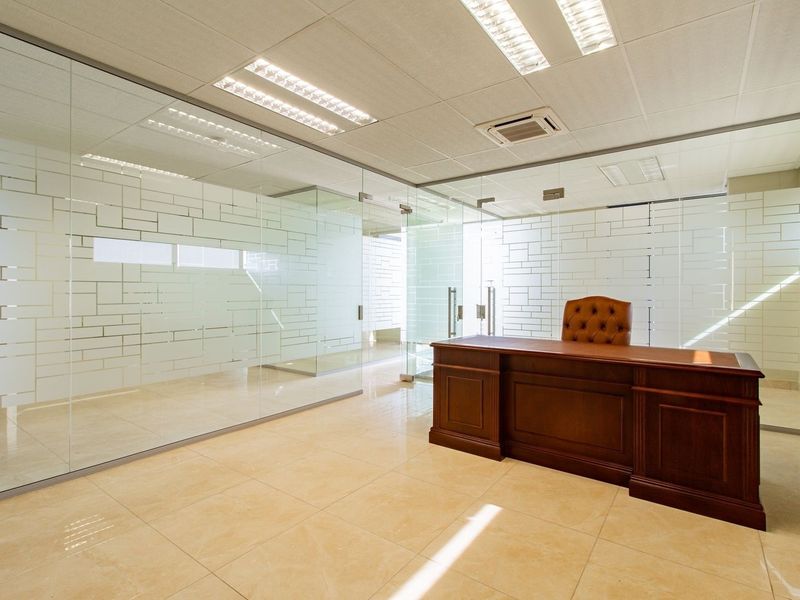 Modern commercial office space featuring glass partition walls with frosted detailing, ceramic tiled flooring, and integrated ceiling lighting.