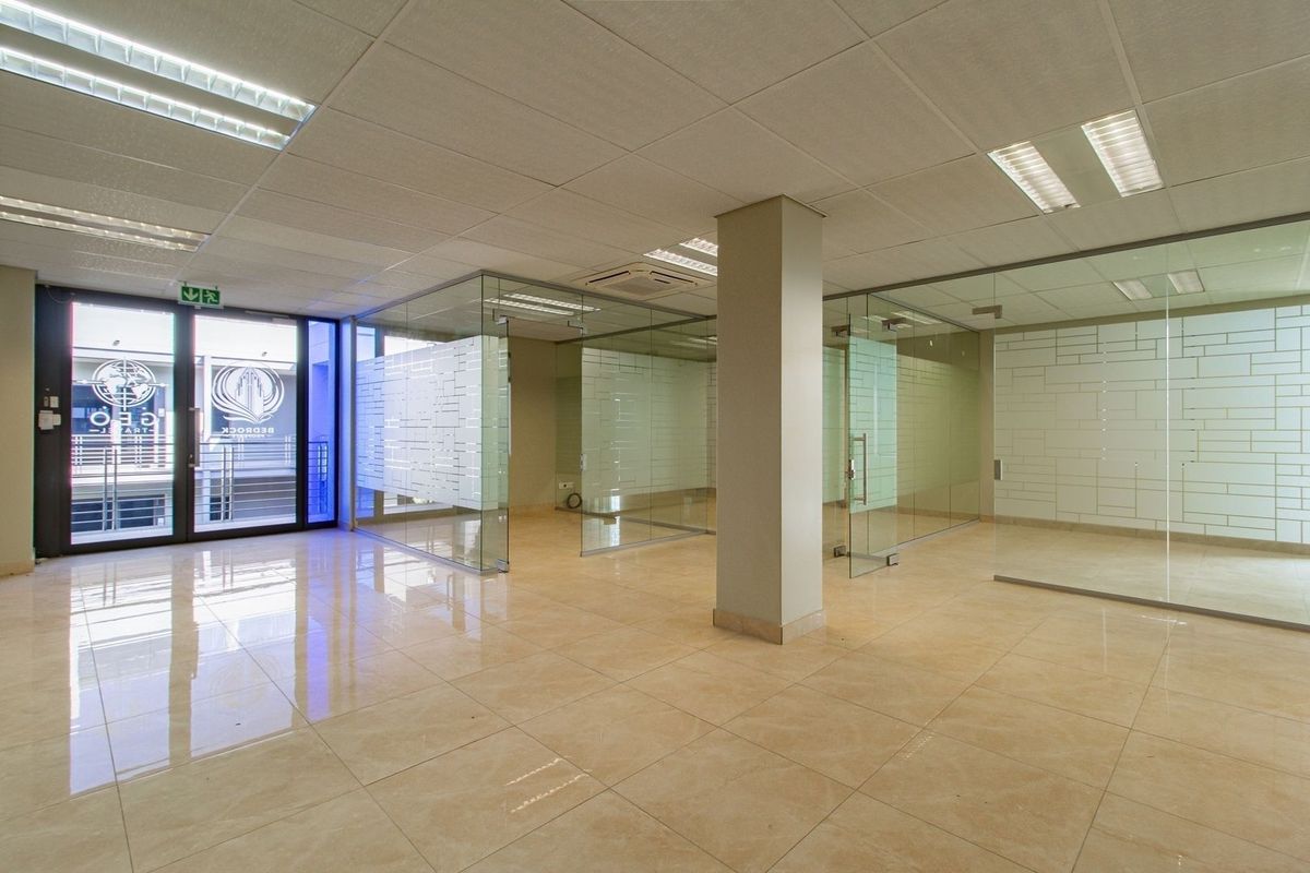 Modern commercial office space featuring glass partitioning, tiled flooring, and a suspended ceiling with integrated lighting, offering a clean and professional open-plan layout.