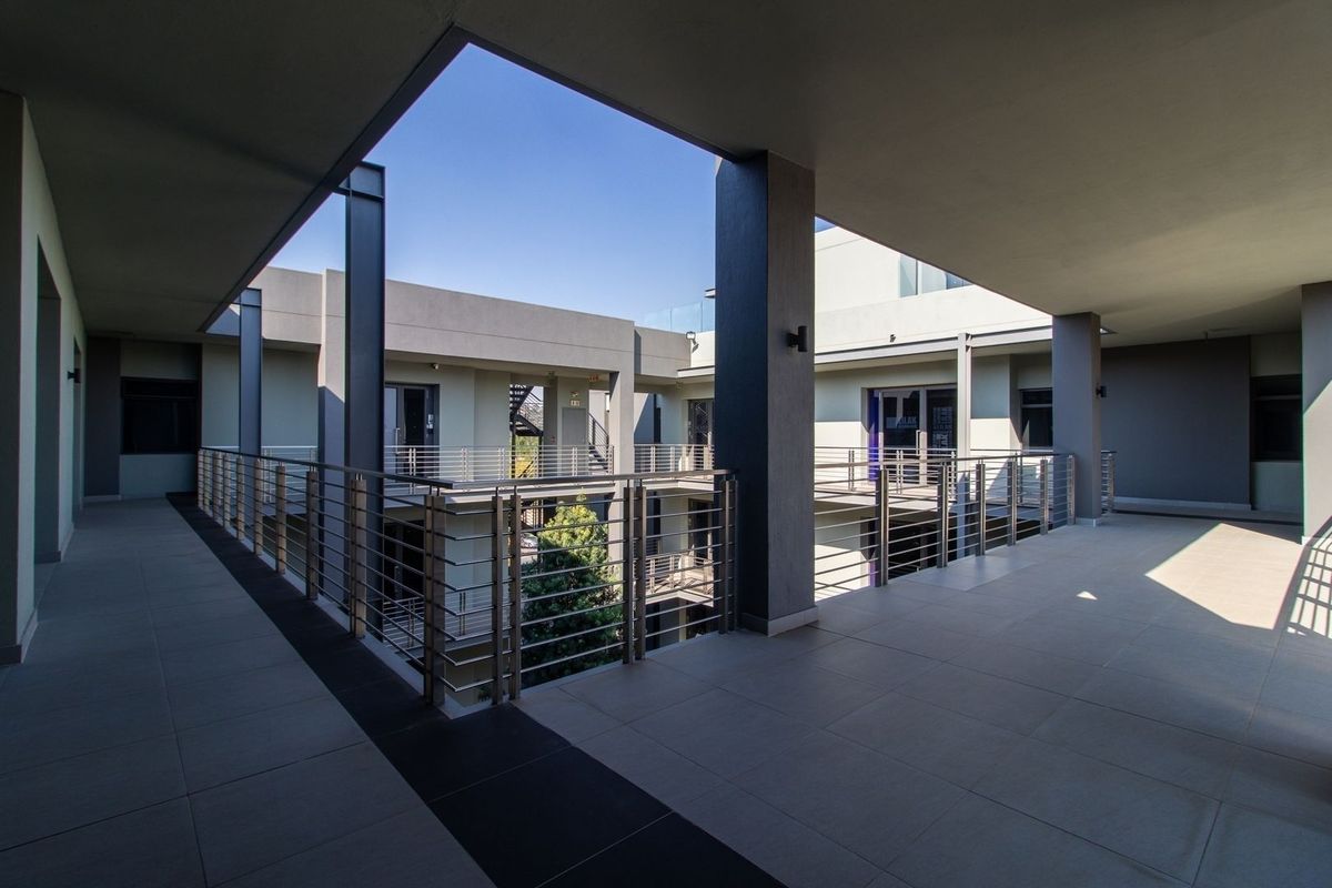 A modern, well-maintained commercial building exterior featuring a spacious covered balcony with stainless steel balustrades and tiled flooring overlooking a central courtyard.