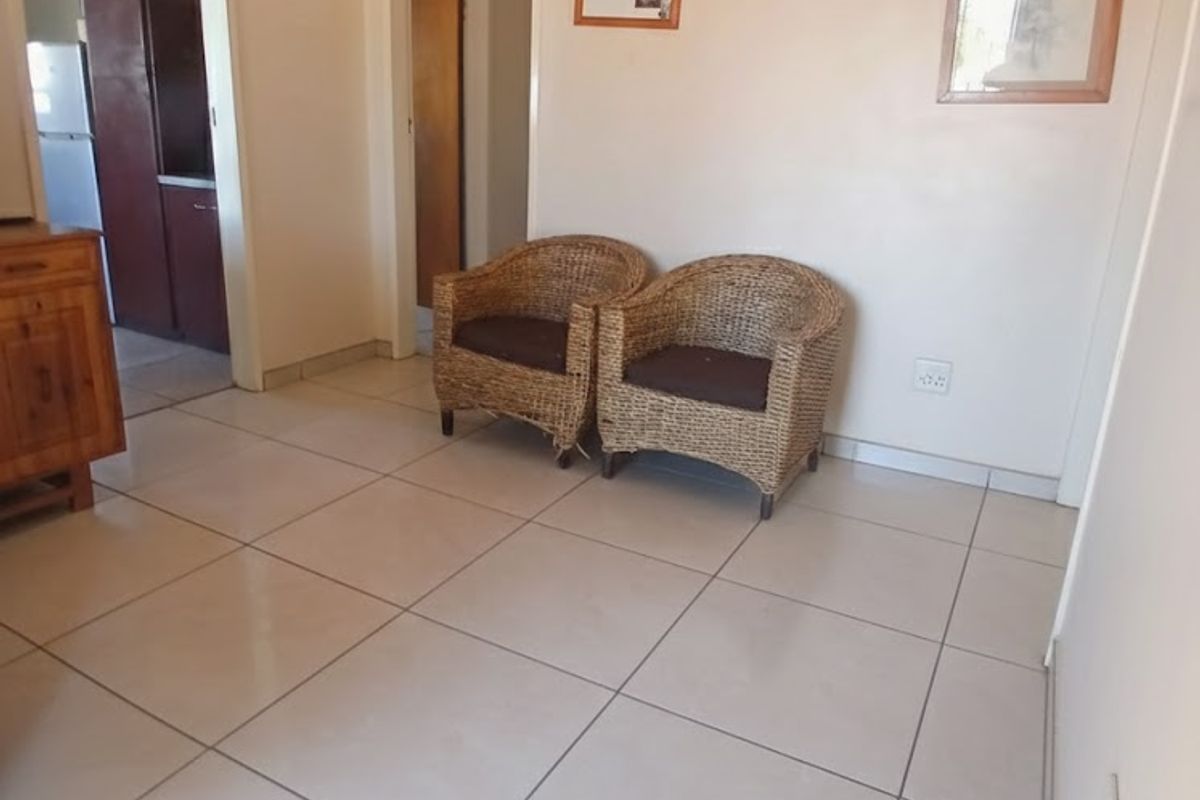 A simple living area featuring neutral ceramic floor tiles and plain walls, providing a functional and clean space with access to adjacent rooms.