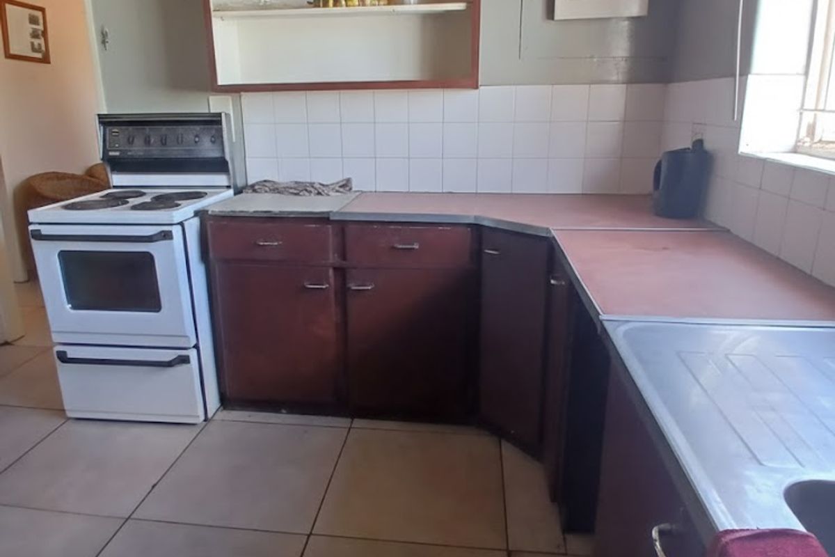 A dated kitchen featuring original cabinetry, laminate countertops, a stainless steel sink, and a freestanding stove, offering significant potential for modernization and renovation.