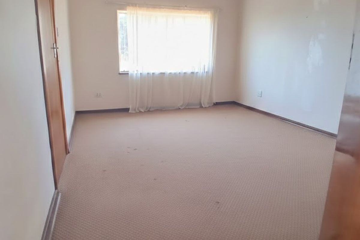 An empty bedroom featuring carpeted flooring, a timber door, and a window with a curtain rail, requiring minor wall and flooring maintenance.