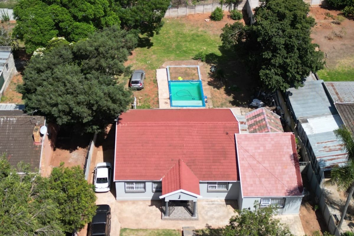 Aerial view of a residential property featuring a tiled roof house, a swimming pool, and a spacious garden area with driveway access.