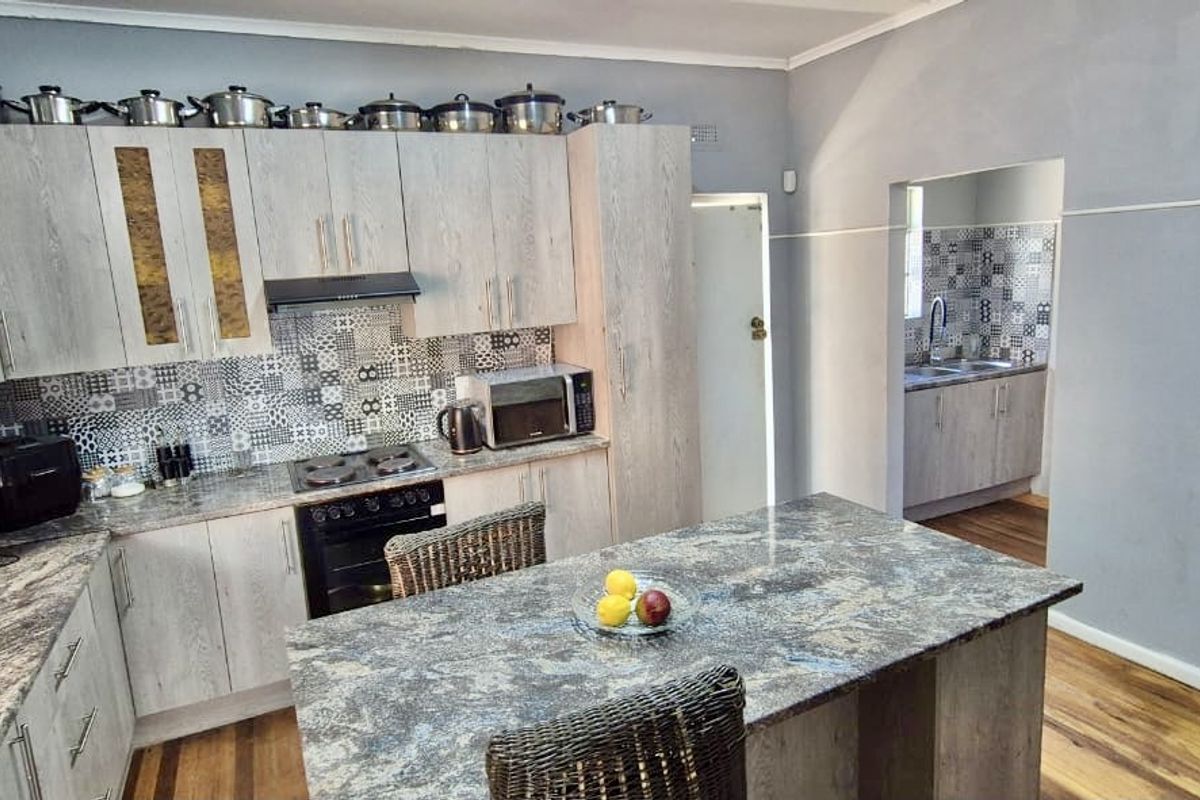 A functional kitchen featuring light wood-finish cabinetry, granite-look countertops, a central island, and a patterned tile backsplash, with an adjacent scullery area.