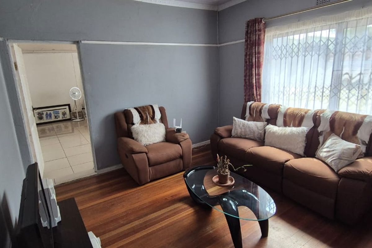 A cozy living room featuring original hardwood flooring, picture rails, and a window fitted with a security gate.