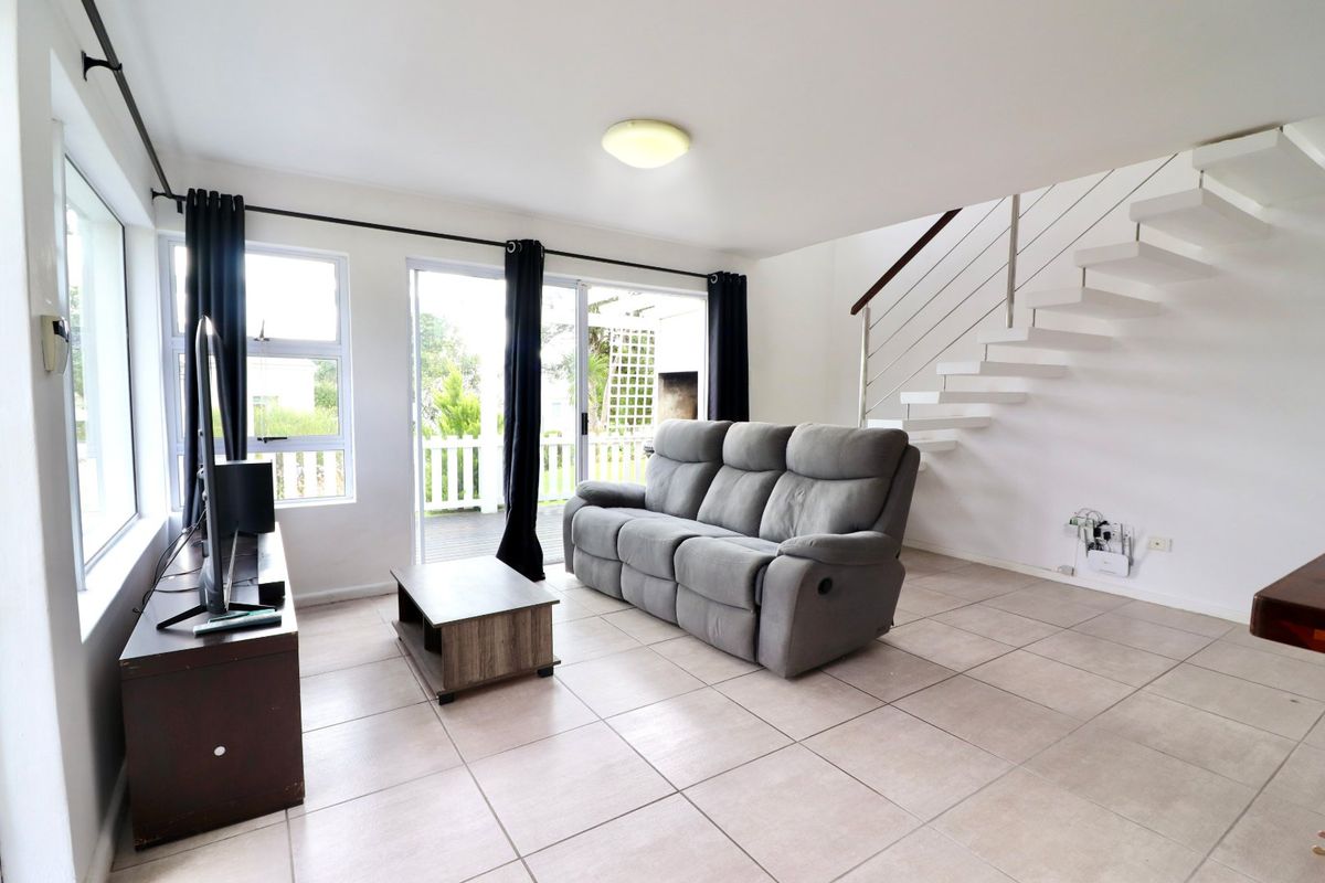 Bright living room featuring tiled flooring, a modern floating staircase with stainless steel balustrades, and sliding glass doors leading to an outdoor area.