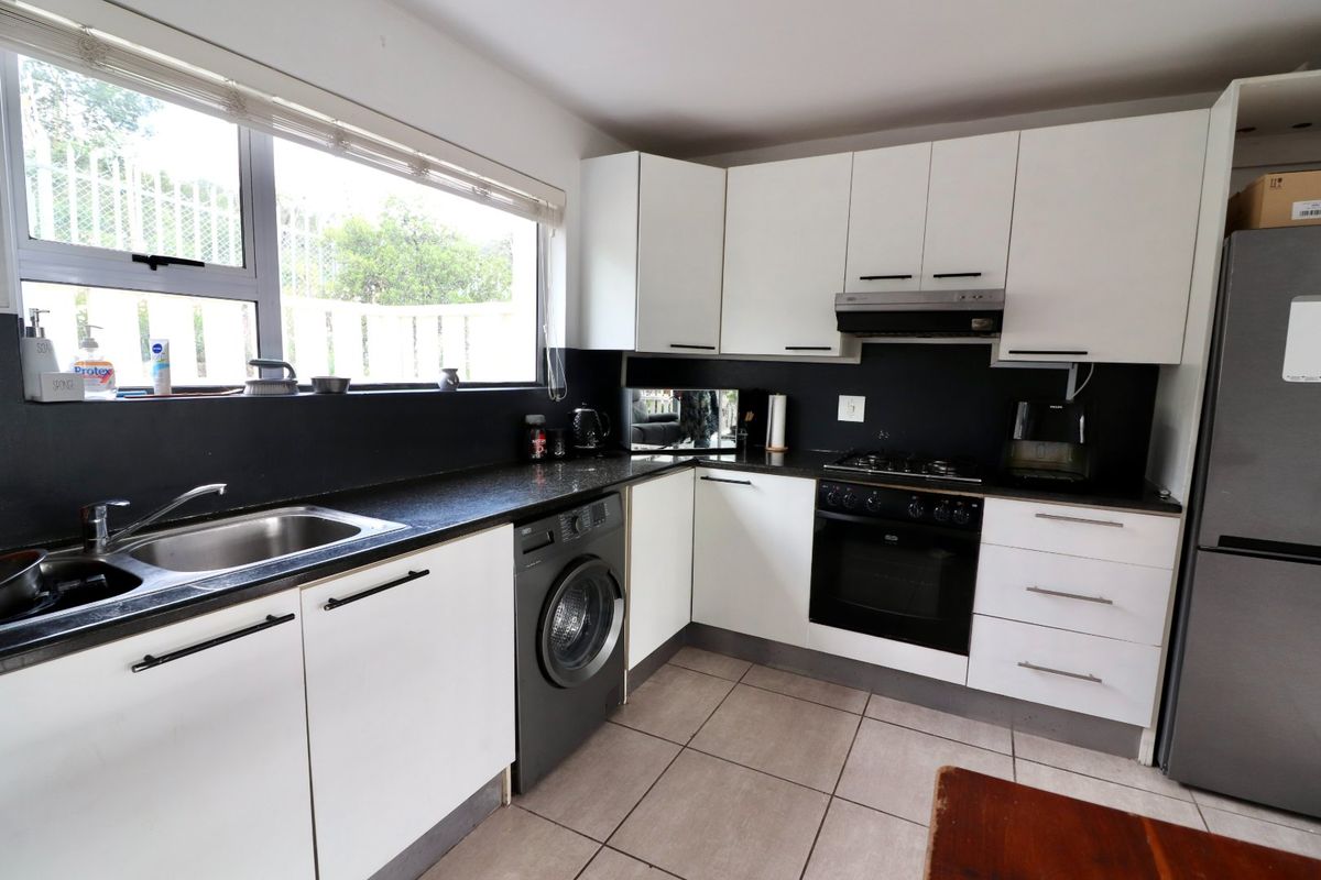 Functional kitchen featuring white cabinetry, dark countertops, tiled flooring, and integrated appliances including a gas hob, oven, and extractor fan.