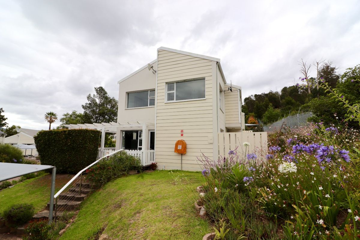 Rear view of the townhouse featuring weatherboard cladding, a pergola, and landscaped garden area with concrete stairs leading to the entrance.