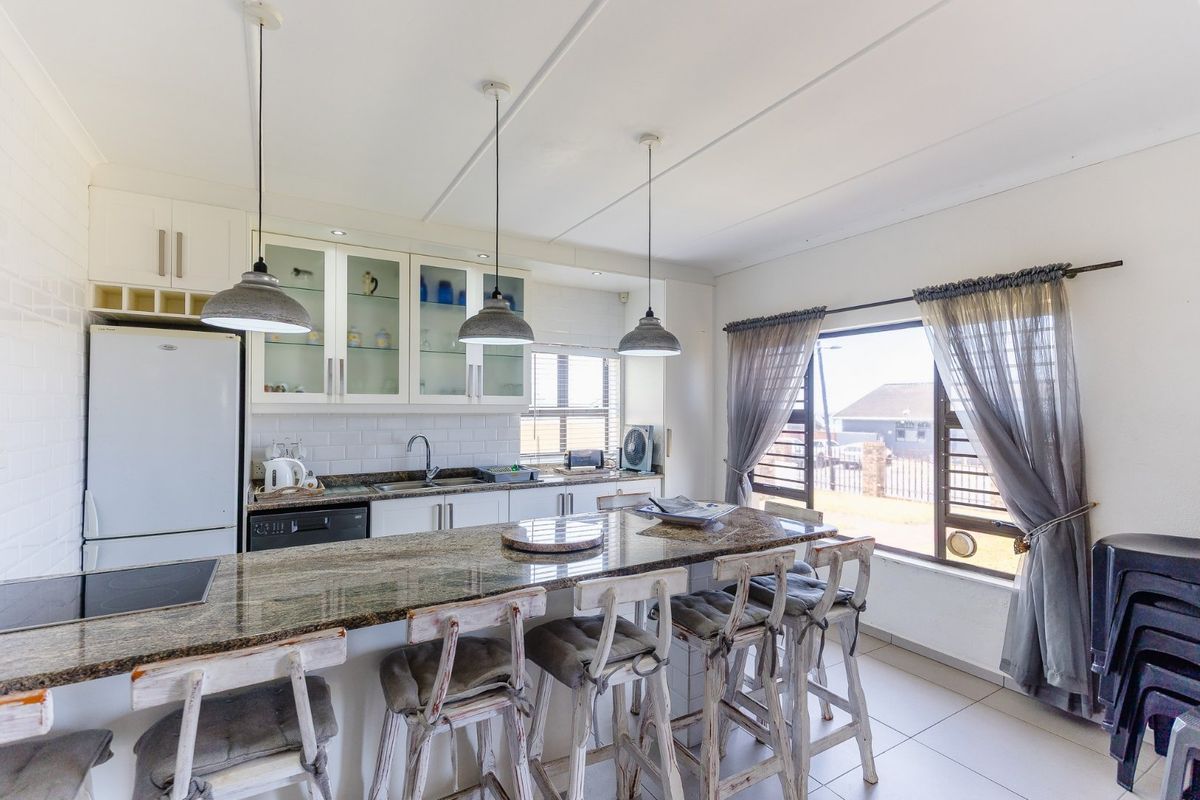 A bright kitchen featuring granite countertops, white cabinetry with glass-front accents, subway tile backsplash, and ceramic tile flooring with ample natural light.