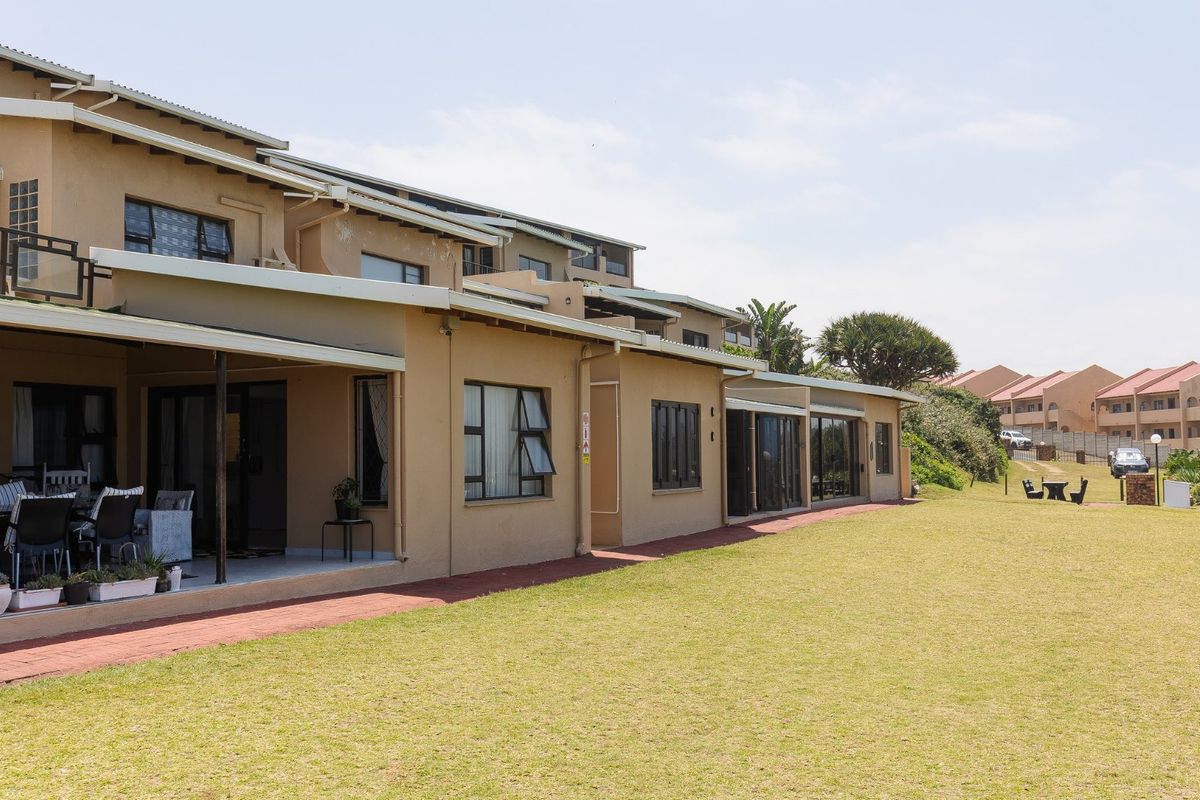 Rear view of the apartment complex featuring a covered patio, paved walkway, and expansive communal lawn area.