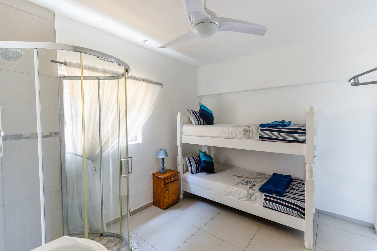 A bedroom featuring tiled flooring, a ceiling fan, and an integrated en-suite shower cubicle.