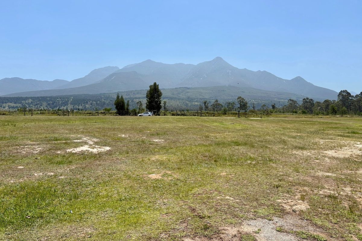 A wide-angle view of a vacant residential plot featuring expansive grassy terrain and scenic mountain vistas in the background.