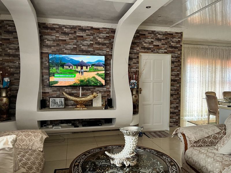 Living room featuring a prominent stone-cladding feature wall with a built-in media unit, tiled flooring, and recessed ceiling lighting.