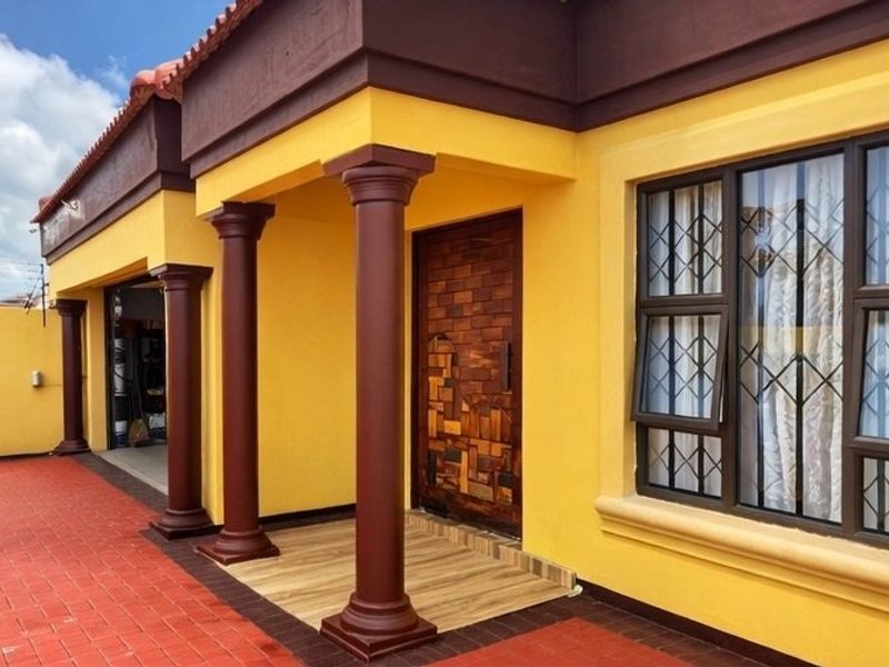 Front entrance of a house featuring decorative columns, a tiled porch, and a unique wooden front door with security bars on the windows.