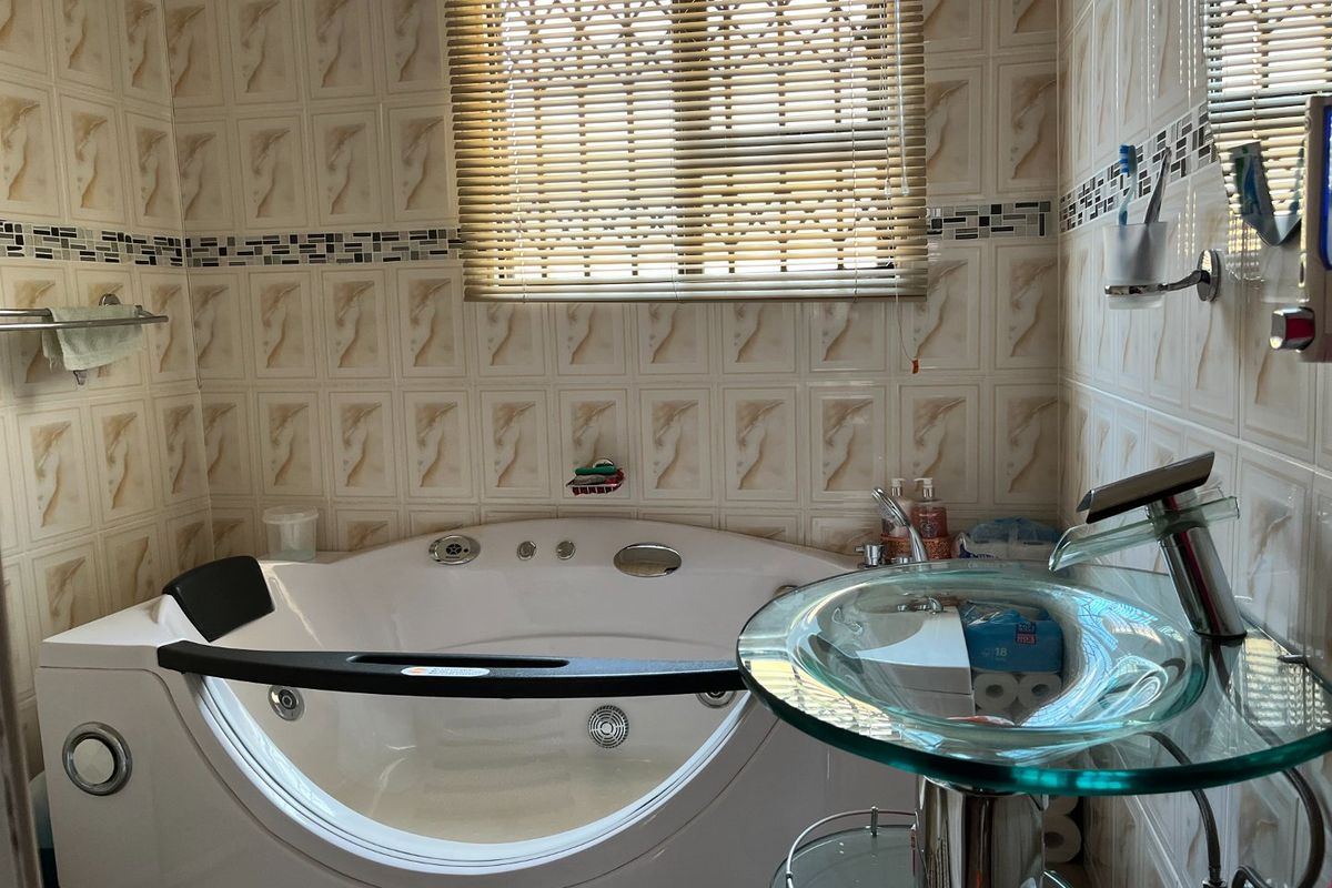 Bathroom featuring a corner spa bathtub, glass vessel sink, and decorative wall tiling with a fitted window blind.