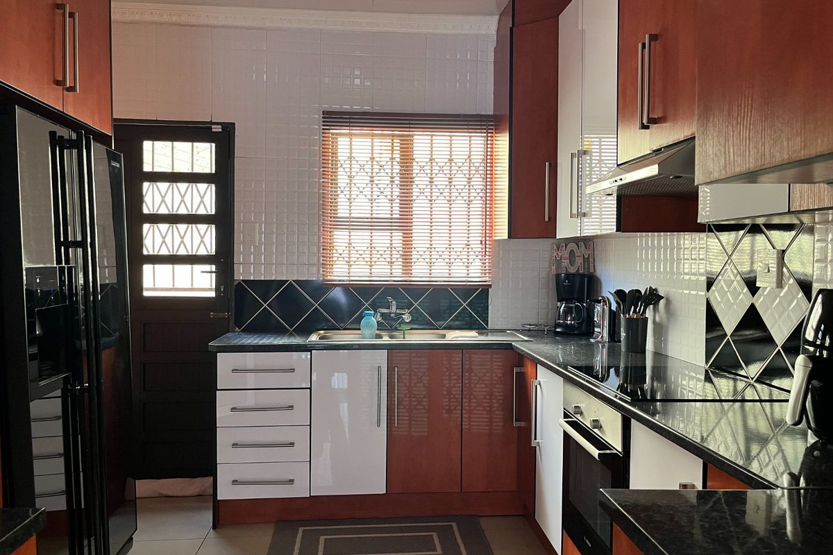 A functional kitchen featuring two-tone cabinetry, granite countertops, a built-in oven, and a tiled backsplash with a secure exterior door.