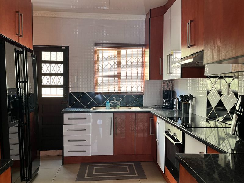 A functional kitchen featuring two-tone cabinetry, granite countertops, a built-in oven, and a tiled backsplash with a secure exterior door.