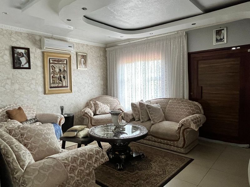 A comfortable living room featuring a recessed ceiling with integrated downlights, tiled flooring, and a wall-mounted split-system air conditioner.