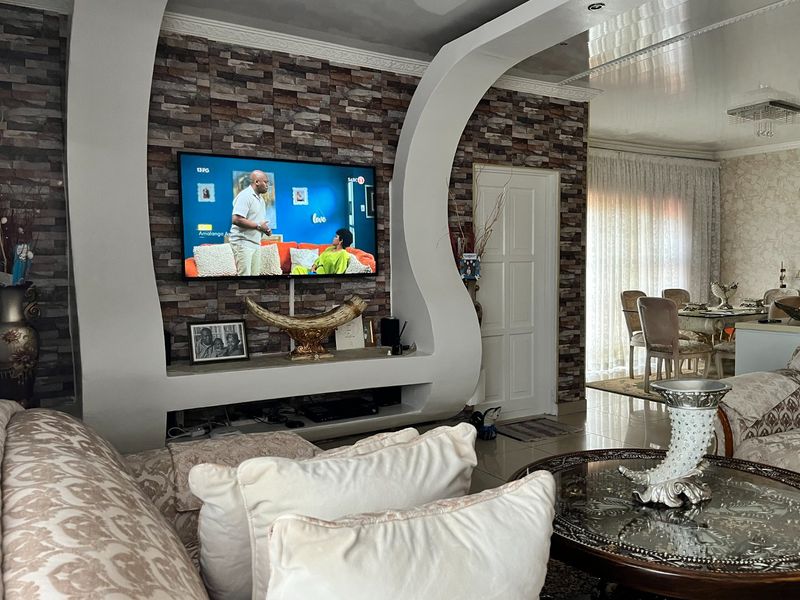 A living room featuring a custom curved built-in media unit, stone veneer feature wall, and glossy ceiling finish with integrated lighting.