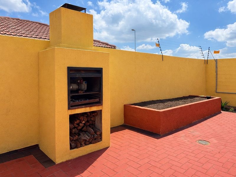 Outdoor patio area featuring a built-in braai, raised garden bed, and paved flooring, enclosed by a perimeter wall with electric fencing.