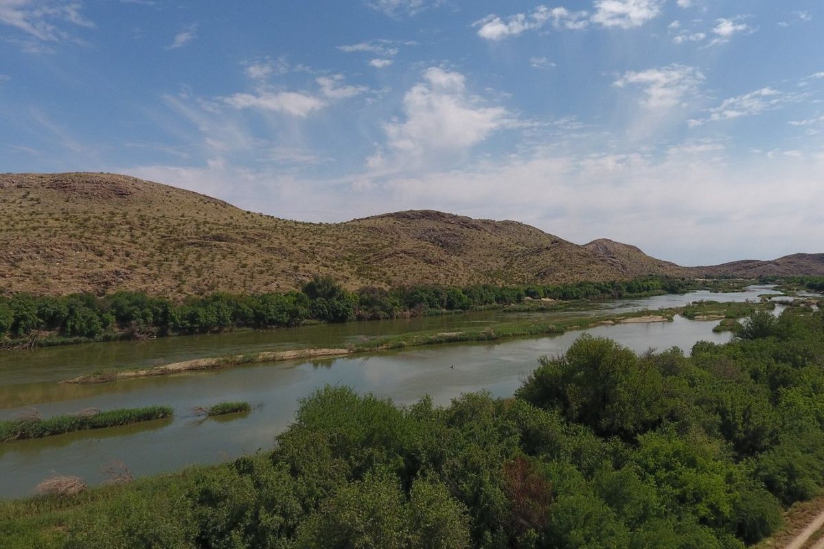 A scenic aerial view of a river flowing through a natural landscape with surrounding hills and lush vegetation.
