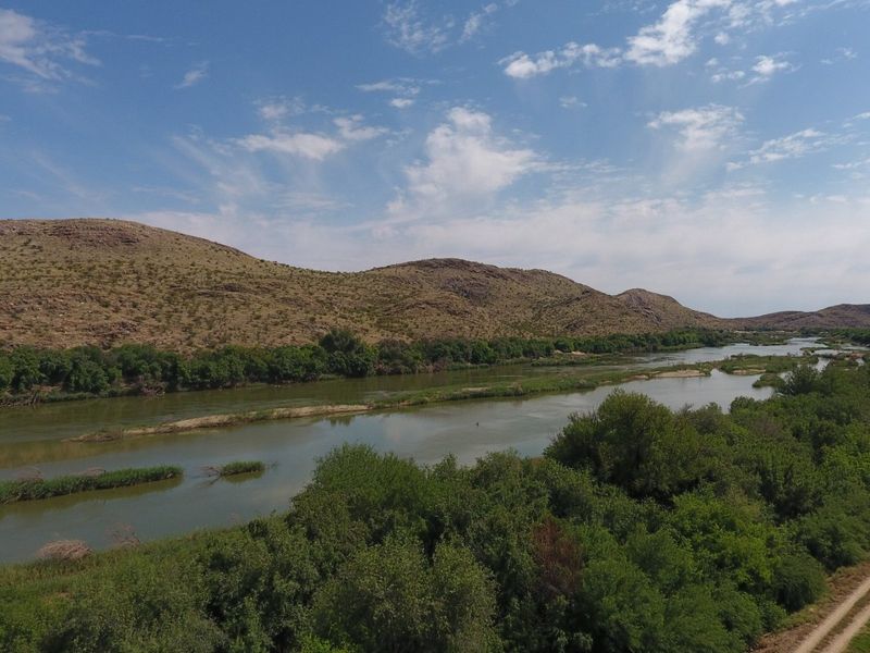 A scenic aerial view of a river flowing through a natural landscape with surrounding hills and lush vegetation.